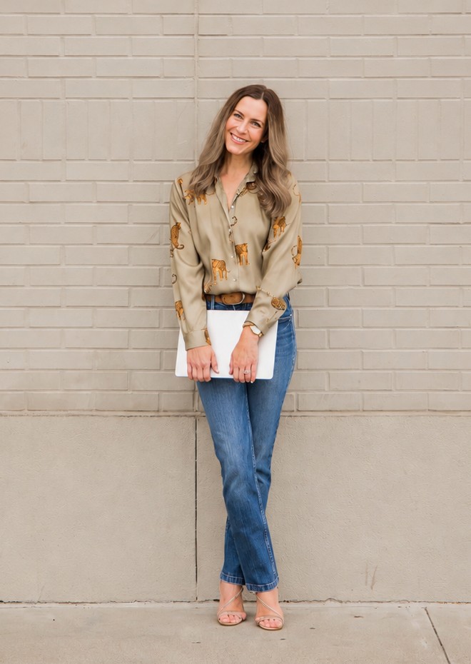 Sarah Boutin standing against a pale brick wall, smiling and holding a laptop